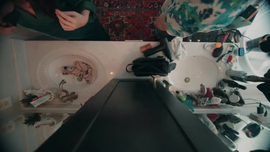 Two people wash up while standing at a double sink in their bathroom
