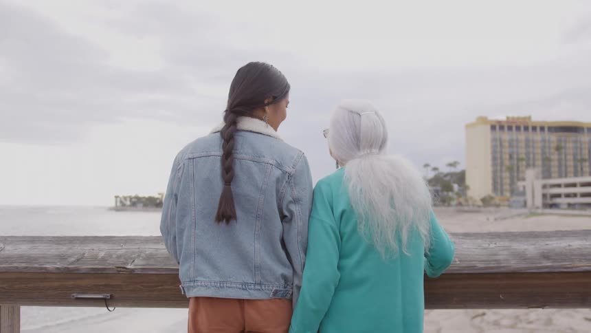 Two native women stand at the railing overlooking a coastal area in the city