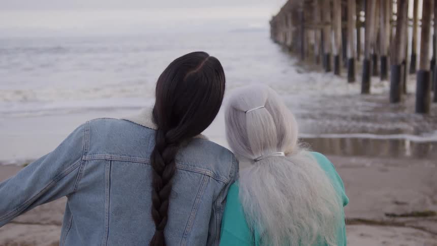 Two women are sitting on the beach looking at the water