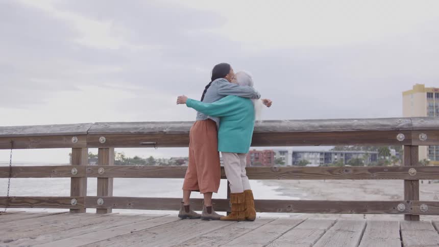 People share a hug on a pier overlooking the beach