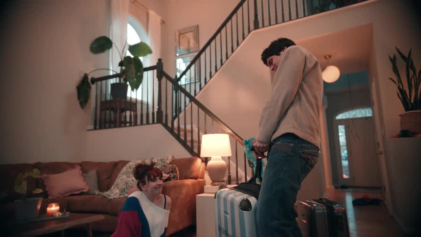 Person sitting on the couch watches someone pulling a suitcase inside a welllit living room