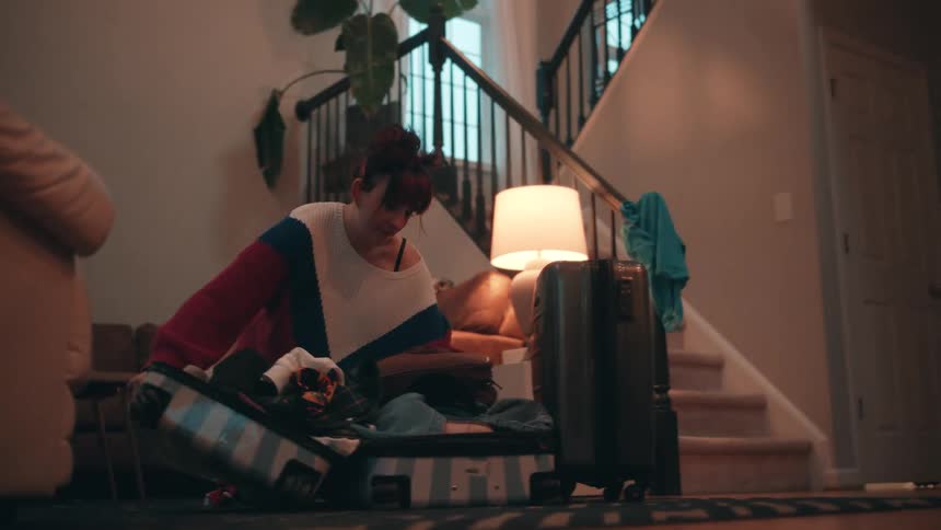 Young adult woman packing clothes on a suitcase in a living room indoors during day time