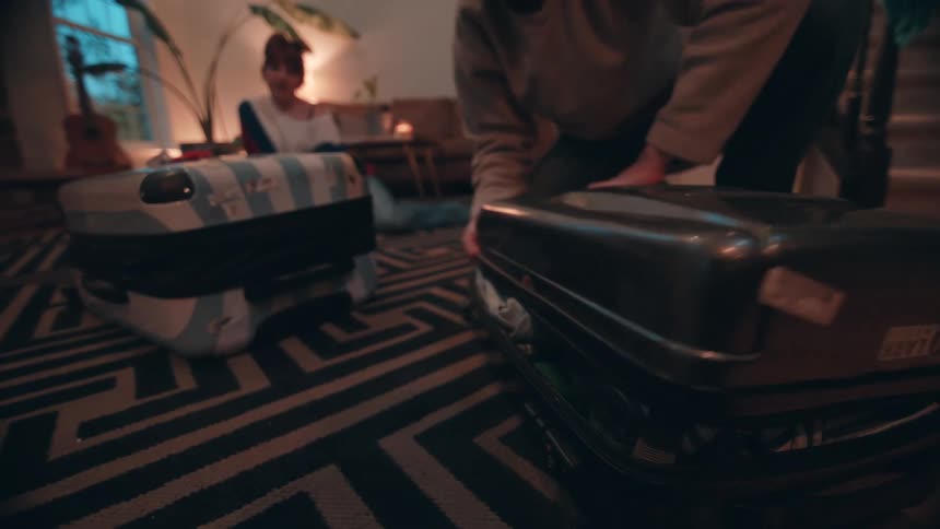 A woman watches as a man tries to shut a suitcase