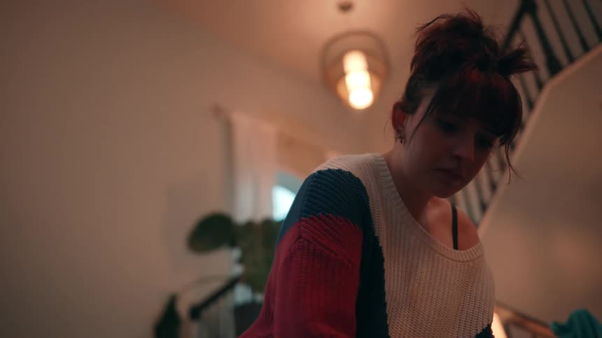 A woman wearing a sweater is rummaging through some clothes in front of her indoors