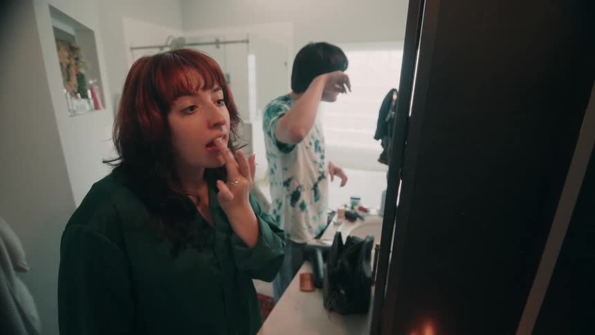 Woman applies makeup while another person gets ready in the bathroom