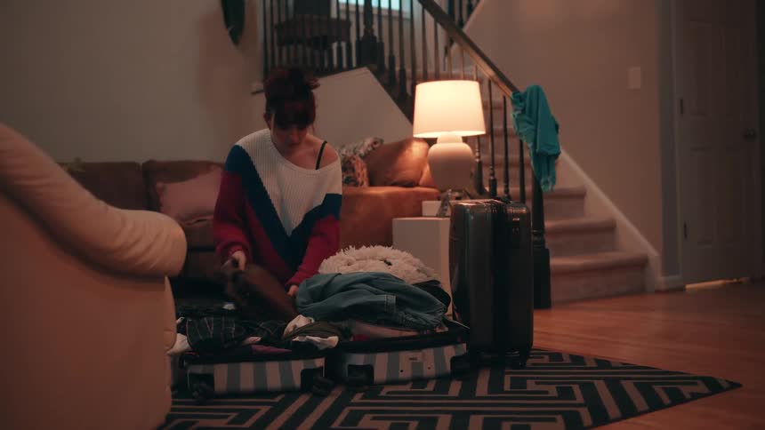 A woman unpacking clothes inside a suit case in the sitting room at night
