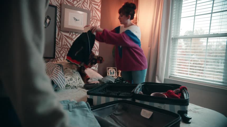 Woman organizes clothes inside an open suitcase on the bed in a bright room