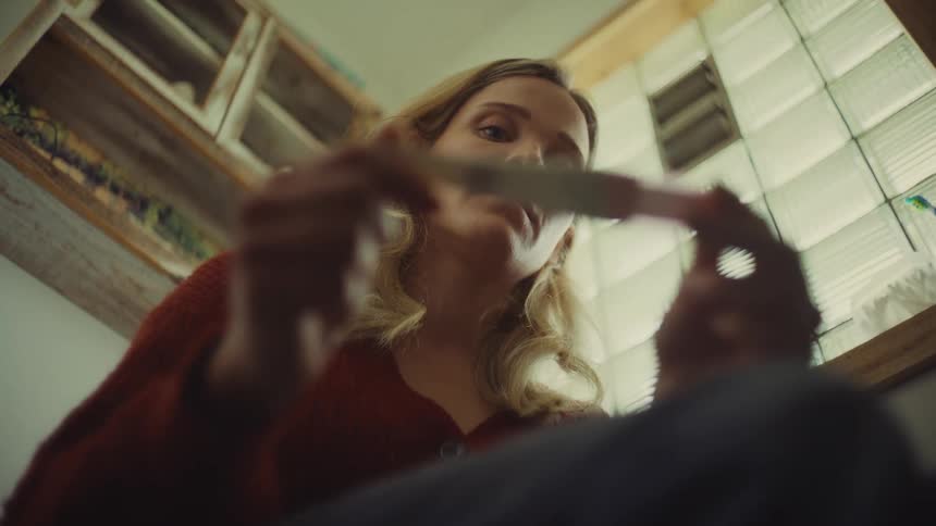 A young woman sits on a toilet seat looking at a pregnancy test tube with surprise