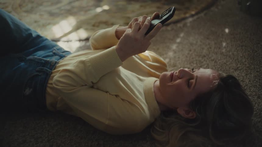 Woman lying on the carpet smiles while using her phone