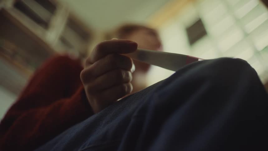 A caucasian female with light hair and a troubled emotion holds a pregnancy test viewed from a low angle inside a room with wooden cabinets