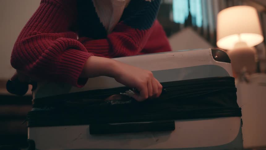 Person struggles to close an overfilled suitcase by pulling the zipper