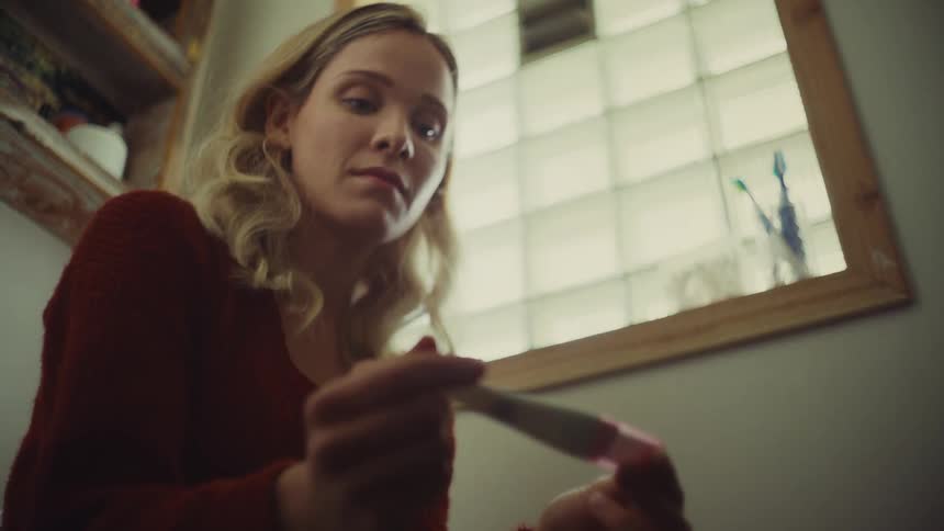 Anxious female holding a pregnancy test in a bathroom