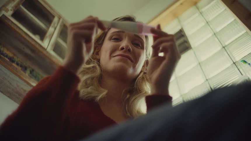 Woman holds a pregnancy test and looks at the result with an emotional expression