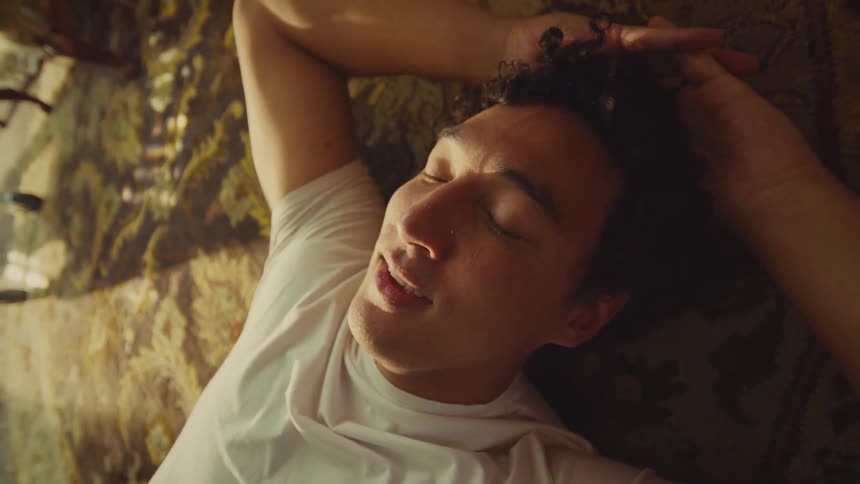 Person in white shirt rests on patterned carpet with arms raised and soft light all around