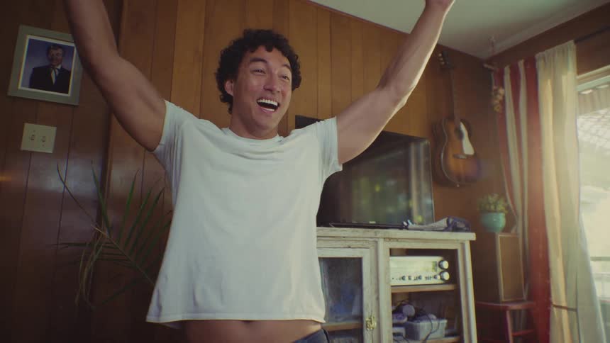 After the woman rolls a pair of dice onto the wooden table the man standing opposite her watches the outcome intently before erupting into a jubilant victory cheer with his arms raised high