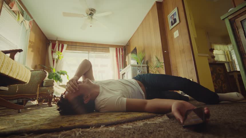 The man rolls on the floor laughing while looking at his phone