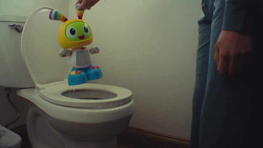 A person wearing dark blue clothing pulls a brightly colored childs toy from a white toilet in a bathroom setting