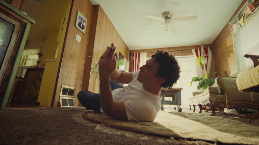 Young man lying down on the floor using a smartphone on his hands before turning over and cheering with intense excitement indoors during day time