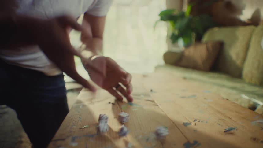 This video begins with a person rolling four dice onto a rustic wooden table with paint splattersthe camera then cuts up to a closeup of a man with curly dark hair and a white tshirt who looks excited and smiles broadly suggesting he has won or ach