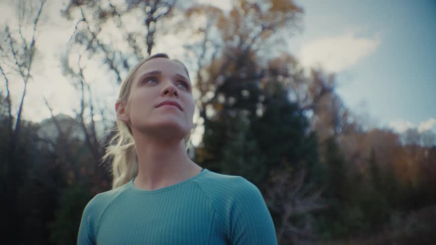 Woman in athletic wear looks up at the sky while walking in a wooded area