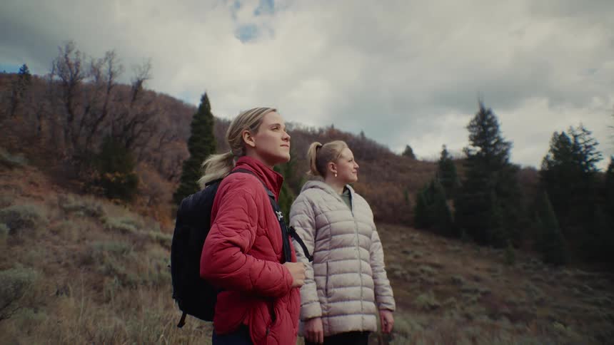 Two women are standing on the side of a mountain looking into the distance