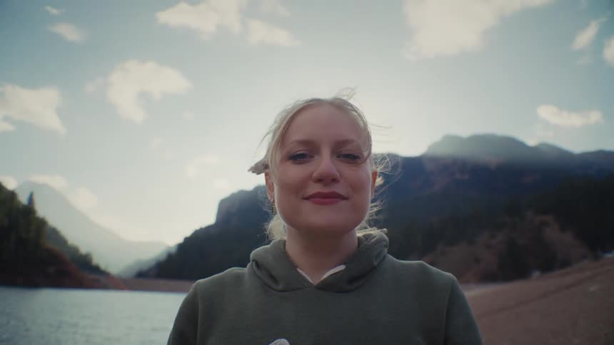 Blonde female standing in wilderness with lake and mountains in the distance