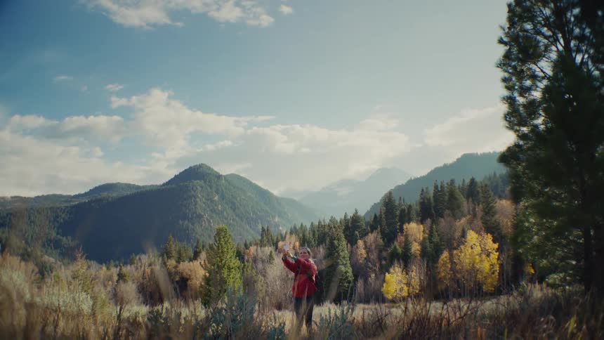 Woman takes a selfie in front of forested mountains under a clear sky