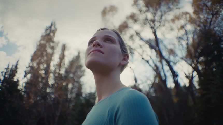 A woman looks at the tops of the trees as she stands in a forest
