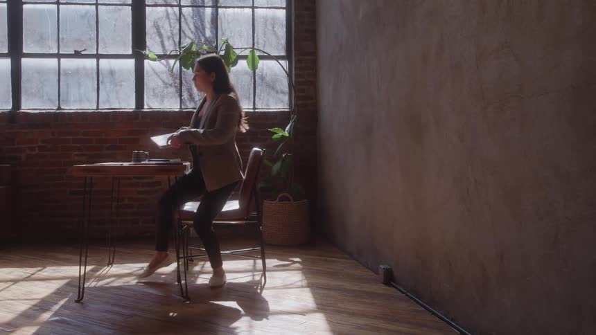 A young woman sits behind a coffee table typing on a computer then stands up closes the lid and walks out of the room