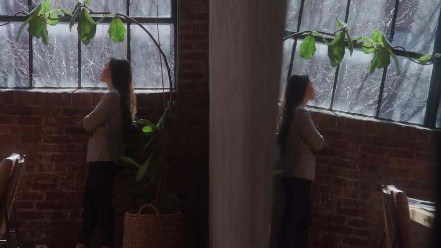 Woman looking out the window in a room with brick walls