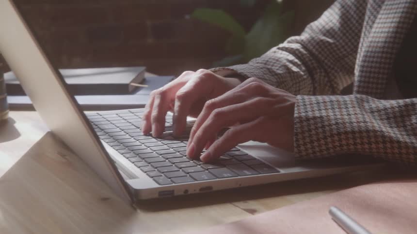Woman sits at a desk typing on a laptop computer and smiles