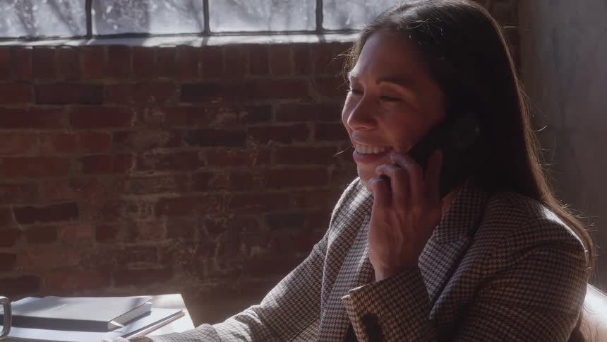 Woman sits at a desk typing on a laptop computer when she stops to answer her phone