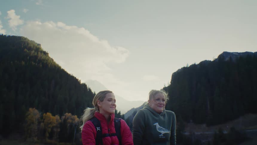 Two smiling women chat and look around at the scenery while taking a break in a mountain valley