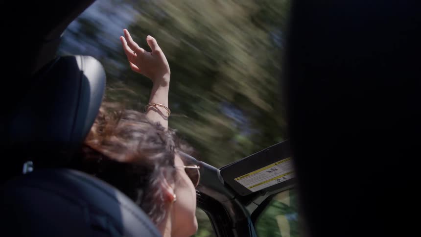 Woman raising her arm and feeling the wind while riding in a convertible car