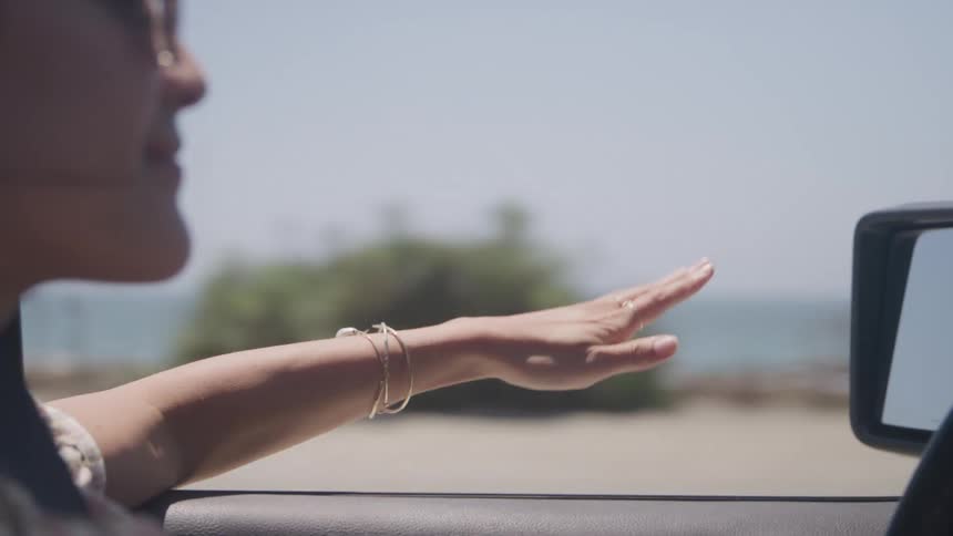 A woman driving a car at midday with her hand sticking out the window