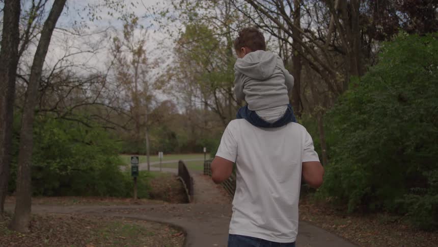 Man walking along a wooded trail carrying a child on his shoulders