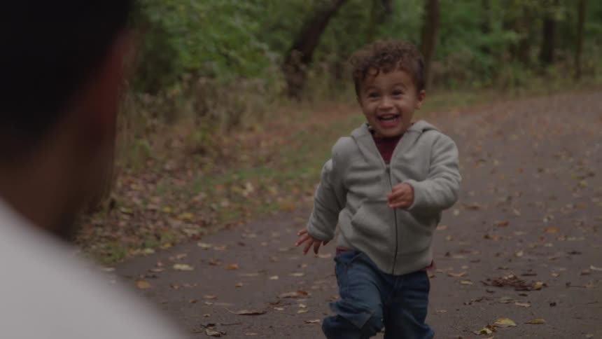 Smiling boy runs toward the person in front of him on a wooded trail