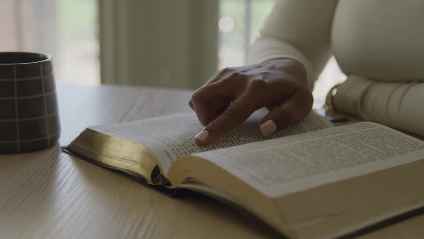 Finger follows the reading in an open book beside a mug