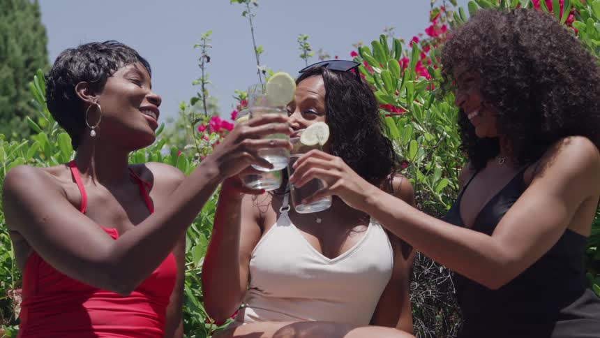 Three woman outside among blooming flowers toasting drinks