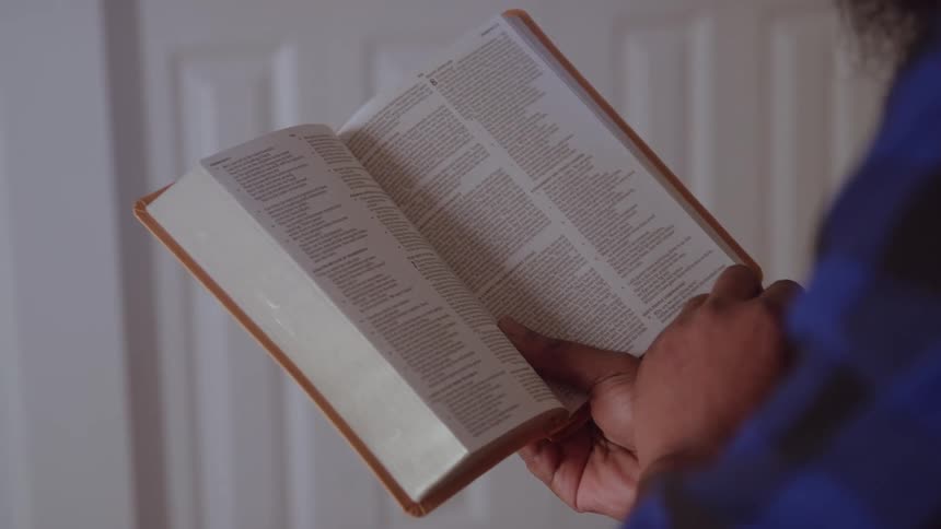 A person holds an open bible using their hand to trace the text while reading