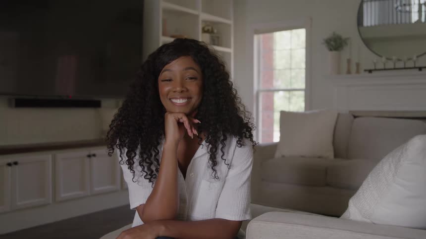 A smiling woman sits on a couch in a modern well lit living room