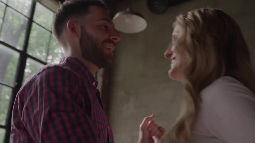 A happy couple affectionately dances and spins together in front of a large window