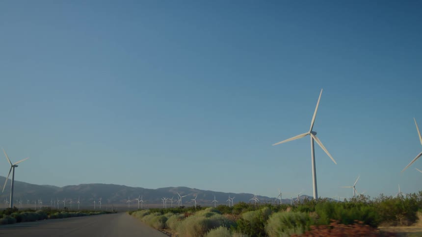 Sunlight shines on turbines spinning on a wind farm