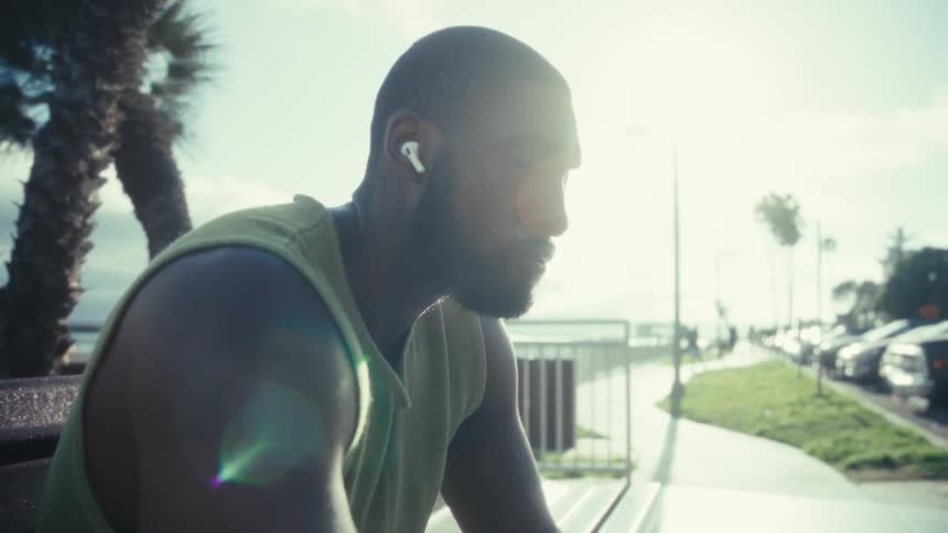 A man is sitting on a park bench listening to his phone as another man walks past