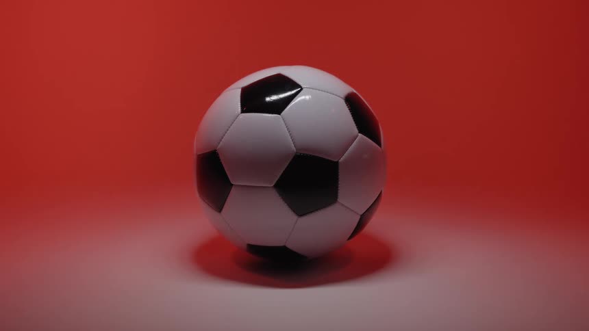 A classic black and white soccer ball in the center of a studio with a bright reddish orange background and soft lighting