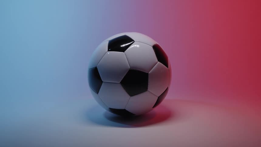 A classic black and white soccer ball spins slowly in the center of a studio with red and blue colored lighting