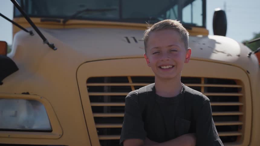 Smiling boy poses in front of a yellow school bus in daylight