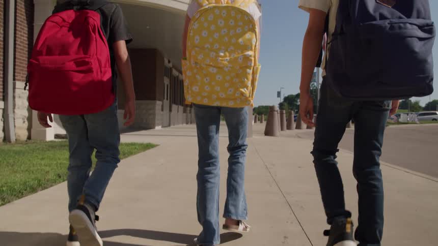 Children walk toward the school wearing colorful backpacks