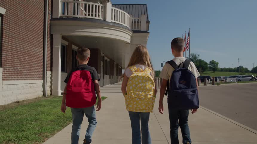 Children walk toward the school entrance with colorful backpacks