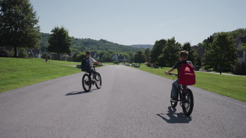 Boys ride bicycles along a quiet street lined with homes and green spaces